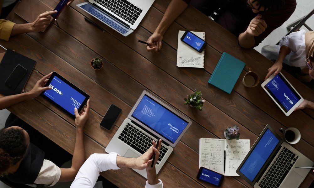 Pessoas sentadas em uma mesa usando notebooks e celulares