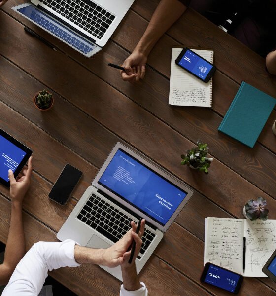 Pessoas sentadas em uma mesa usando notebooks e celulares